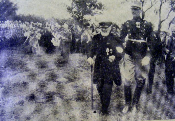 Mathias Sørensen, støttet af oberstløjtnant Holnæs, skridter fronten af. Billedet er fra et avisudklip. 